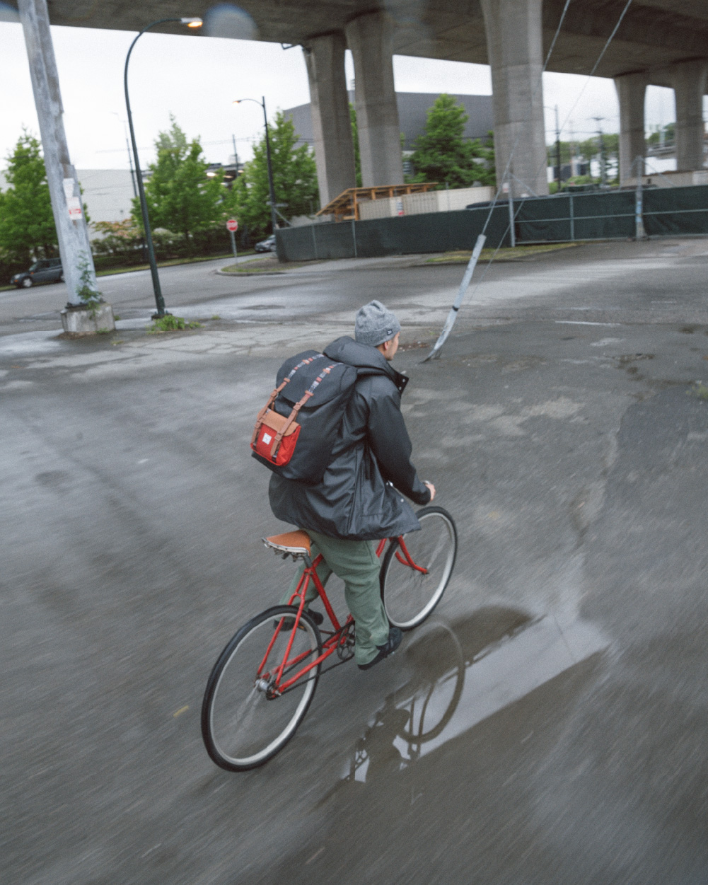 A person riding their bike under metro tracks while wearing their Herschel Little America Backpack.